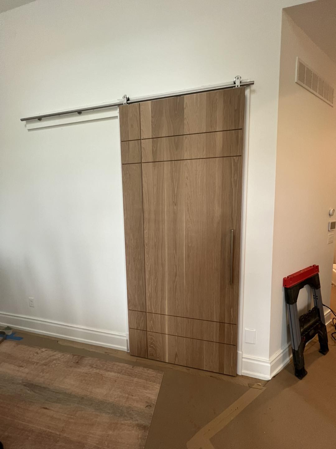 Custom modern wood sliding barn door installation by Ruach Custom Carpentry in Columbus, Ohio, featuring a minimalist slab-style design with horizontal accent lines and a sleek metal track system. This custom carpentry project highlights expert finish carpentry, custom door craftsmanship, and contemporary woodwork, adding functional elegance and architectural style to a luxury Central Ohio home.