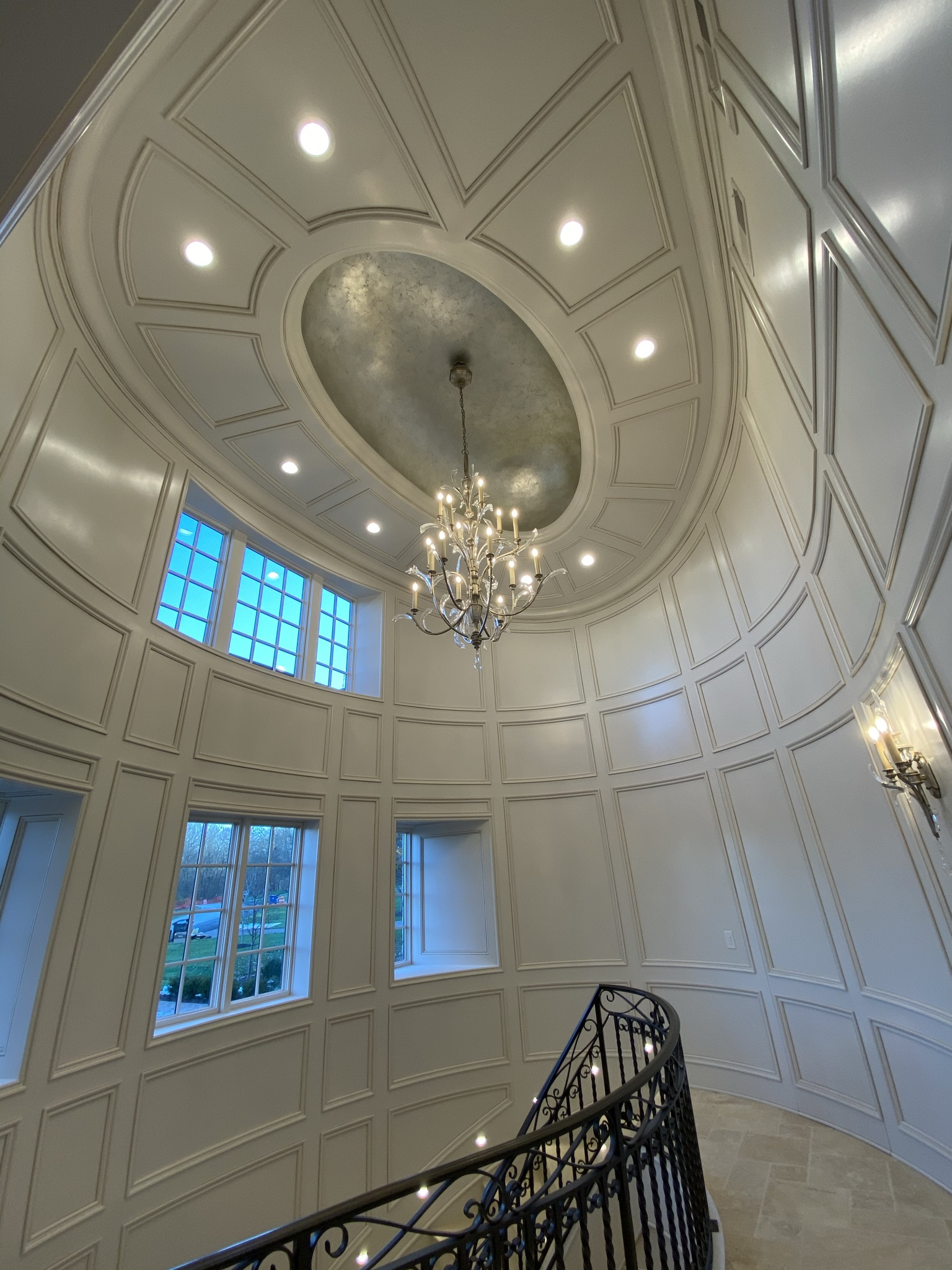Custom curved wall paneling and decorative ceiling trim installation by Ruach Custom Carpentry in Columbus, Ohio, featuring elegant handcrafted wood panels, detailed crown molding, an oval recessed ceiling with metallic finish, and a grand staircase with wrought iron railing. This luxury carpentry project highlights expert finish carpentry, custom woodwork, and precision craftsmanship, creating an impressive architectural centerpiece in a high-end Central Ohio home.