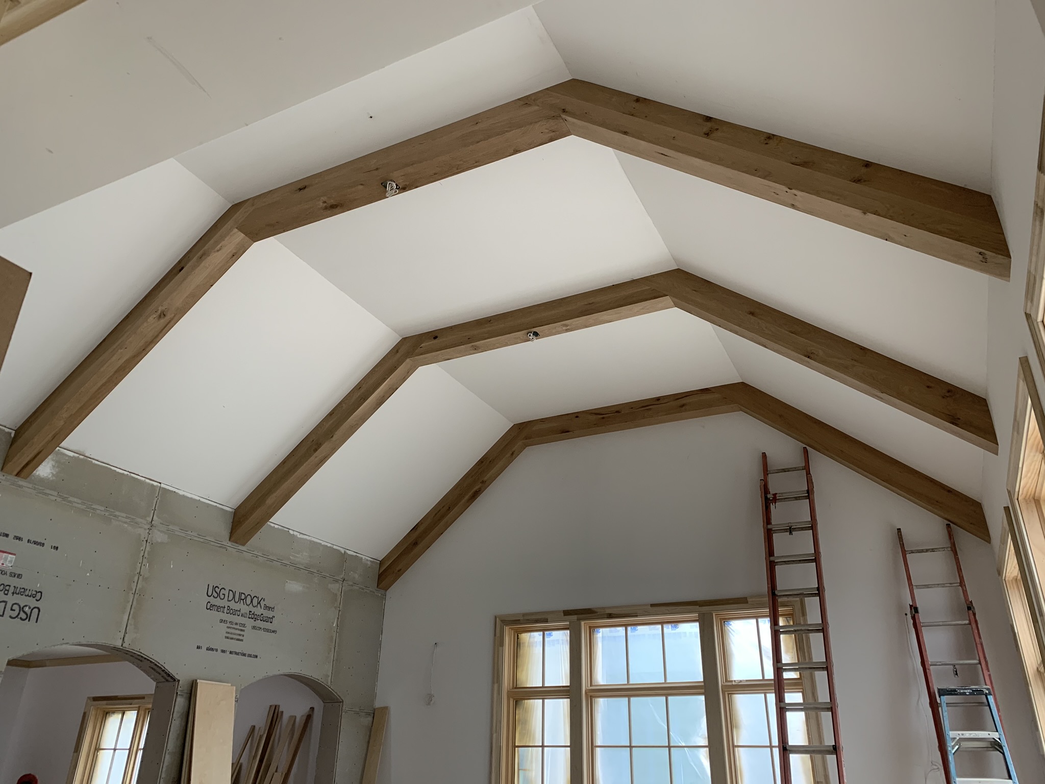 Custom vaulted ceiling with exposed stained wood beams, showcasing expert carpentry craftsmanship by Ruach Custom Carpentry. The natural wood beams create a warm, architectural focal point in the bright, airy living space.