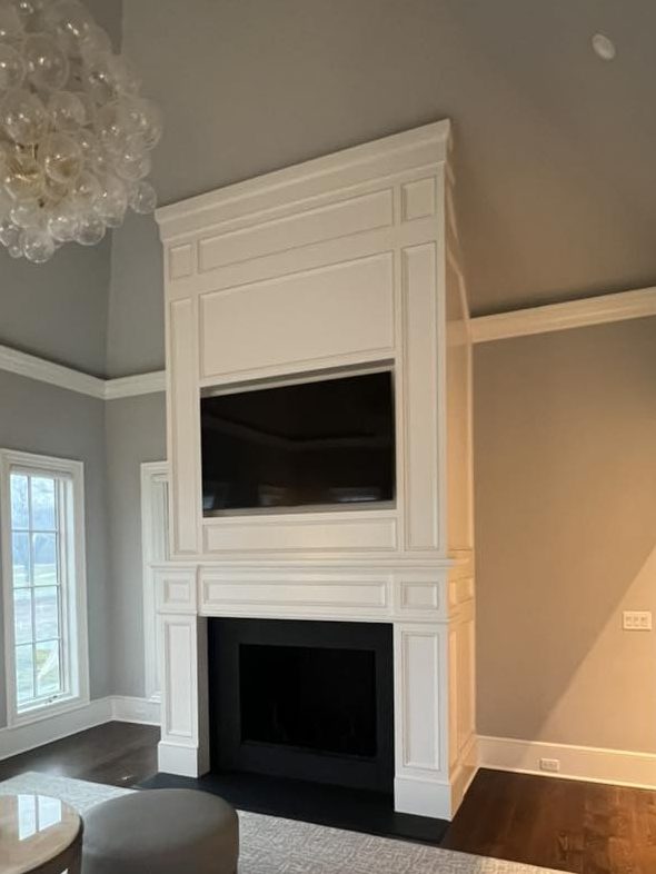 Custom fireplace surround with integrated TV frame and detailed paneling by Ruach Custom Carpentry in Columbus, Ohio. This handcrafted fireplace features intricate millwork, classic trim details, and a modern, built-in TV niche, blending traditional craftsmanship with a clean, high-end design. A stunning centerpiece for a luxury living room, showcasing expert finish carpentry and custom woodwork in Central Ohio.