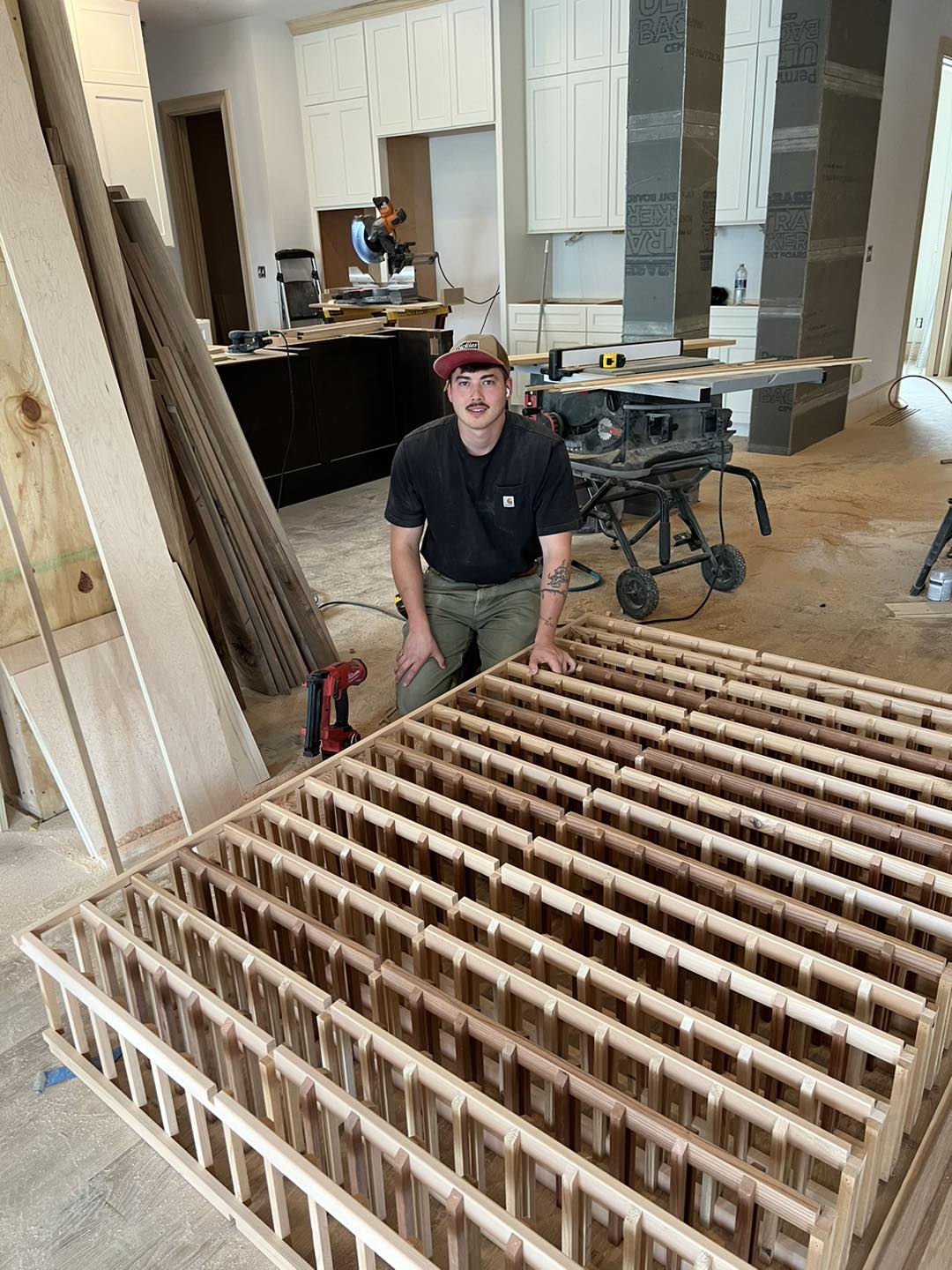 Daniel Mackamul, Head Carpenter and Project Director at Ruach Custom Carpentry in Columbus, Ohio, kneeling beside part of a handcrafted custom wood wine cellar in a home, showcasing expert finish carpentry, built-ins, and fine woodworking.